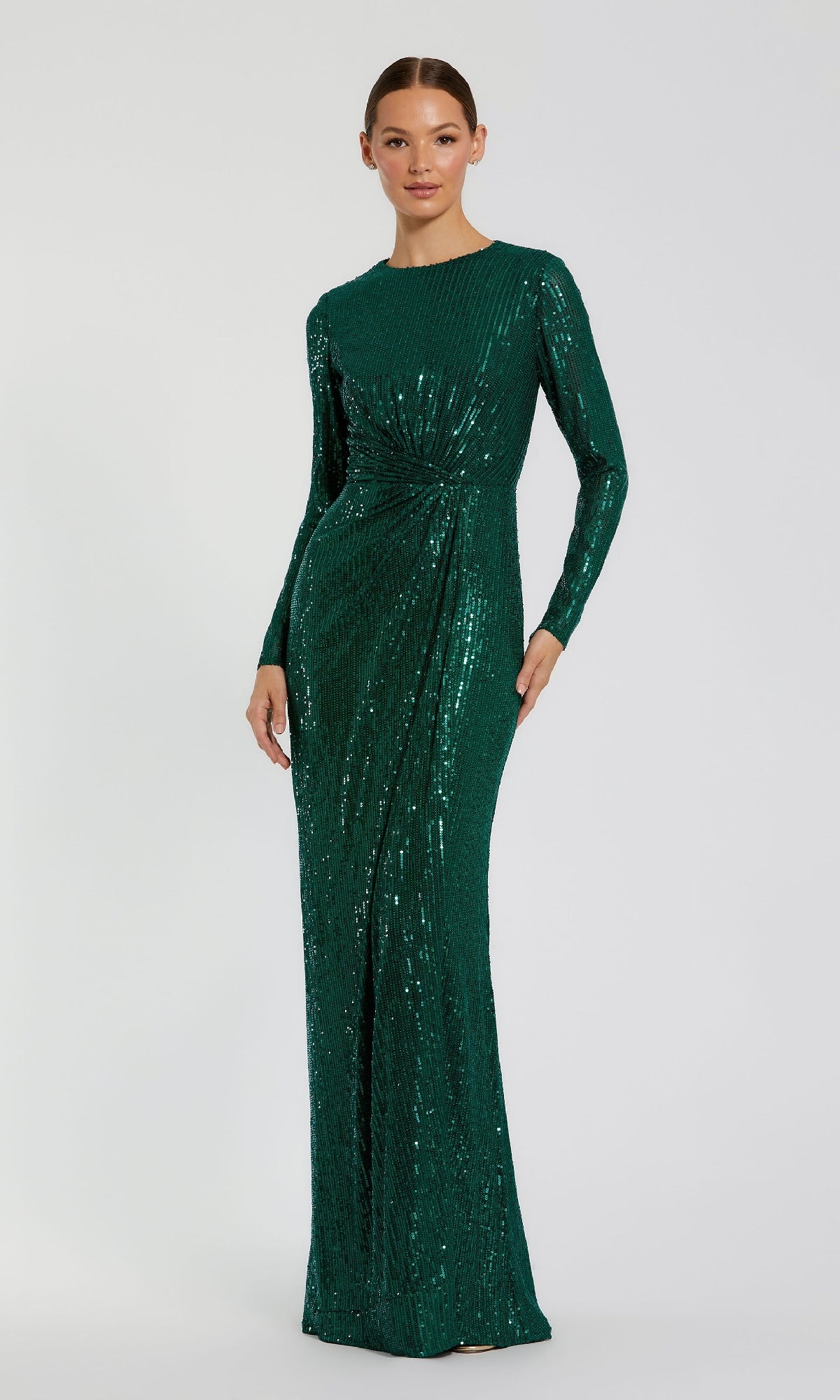 A woman wears the Mac Duggal 11659 long sleeve sequin formal dress—an elegant, floor-length emerald green gown featuring a waist knot detail.